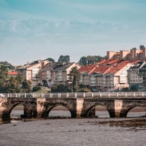 Picturesque view of a historic bridge and vibrant buildings in Cambre, Galicia, Spain under a clear blue sky.
